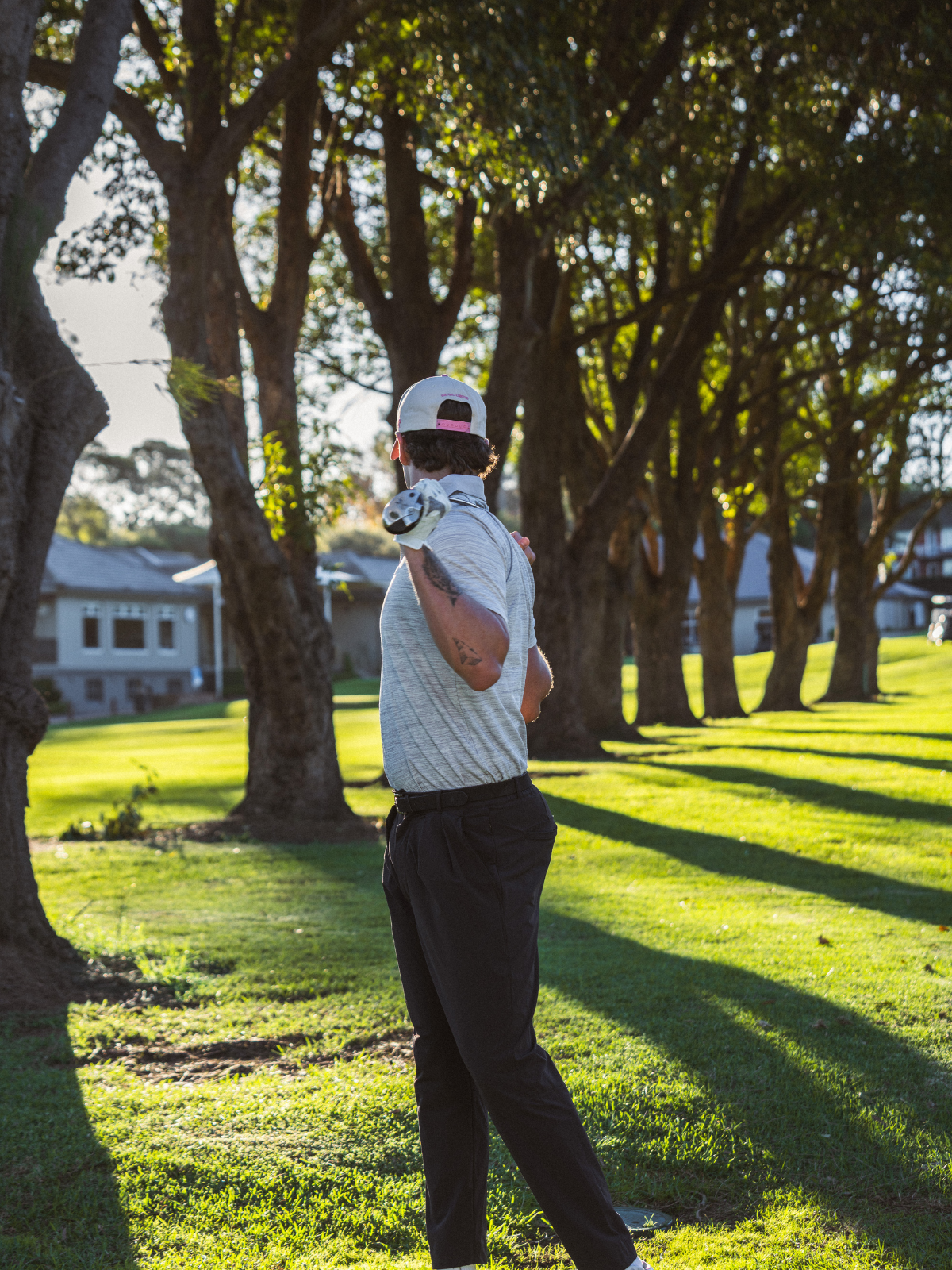 Man wearing Public Drip Frequency Polo in grey, back view on tree-lined golf course fairway
