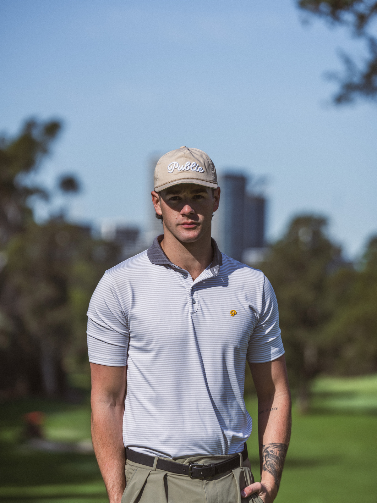 Man wearing Public Drip Public Athlete Striped Polo in white, front shot on golf course with city skyline