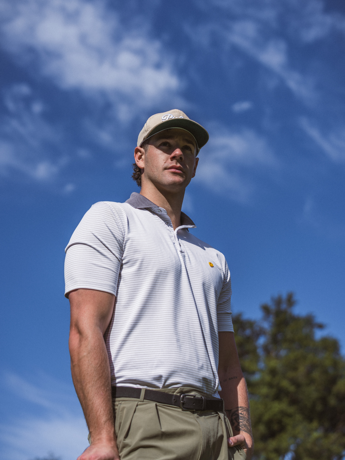 Man wearing Public Drip Public Athlete Striped Polo in white, low angle editorial shot against blue sky