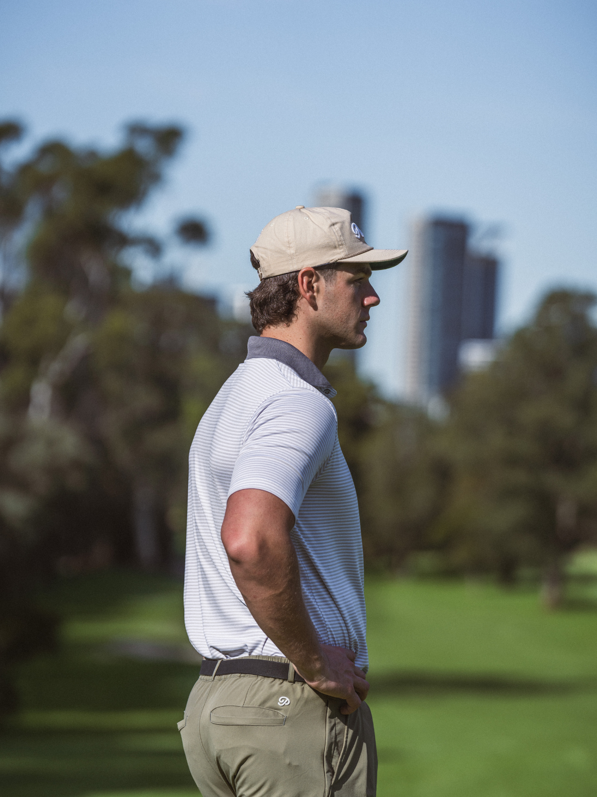 Man wearing Public Drip Public Athlete Striped Polo in white, side profile shot on golf course with city skyline
